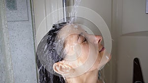 Brunette woman washing in shower watering hair, face with water from shower head