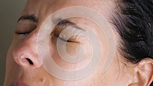 Brunette woman washing in shower watering hair, face with water from shower head