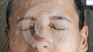 Brunette woman washing in shower watering hair, face with water from showerhead