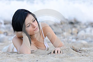 brunette woman, wear wet t-shirt as she lie on sandy beach