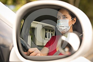 Brunette woman wearing face mask driving her car through the side mirror car. Covid-19 Corona virus