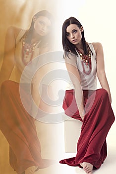 Brunette woman with white shirt, long red skirt and jewellery, sitting in a pose over white, with reflection