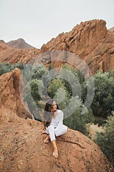 Brunette woman in white sitting and enjoying view of mountain canyon in Morocco