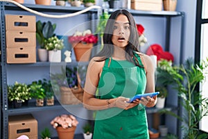 Brunette woman working at florist shop holding tablet afraid and shocked with surprise and amazed expression, fear and excited