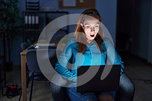 Brunette woman working at the office at night afraid and shocked with surprise expression, fear and excited face