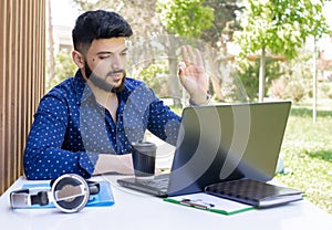 Brunette young male with beard sititng at table, using laptop.