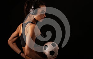 Brunette young strong woman ready to competition in sport clothing and holding basketball ball in wireless headphones in on black