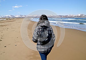 Brunette young woman with backpack walking on the beach close to snowy mountains and Japanese sea. Solo traveller.