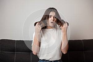 Brunette young woman with damaged long hair and split ends looks desparate and unhappy with her hairstyle, bad hair day concept