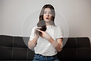 Brunette young woman with damaged long hair and split ends looks desparate and upset with her hairstyle, bad hair day concept