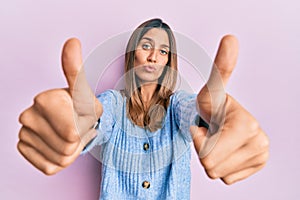 Brunette young woman doing thumbs up positive gesture looking at the camera blowing a kiss being lovely and sexy photo