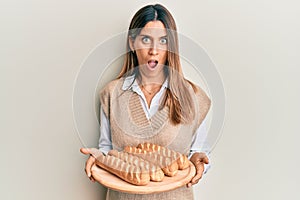 Brunette young woman holding homemade bread afraid and shocked with surprise and amazed expression, fear and excited face