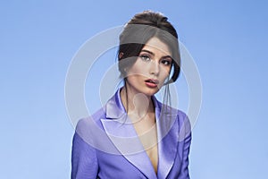 Brunette young woman with makeup and hairstyle in a stylish purple suit, looking at camera, isolated blue background.