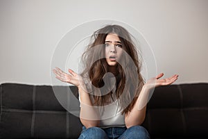 Brunette young woman with tangled long hair looks desparate and unhappy with her hairstyle, bad hair day concept