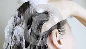 Brunette young woman washing head with shampoo with foam closeup