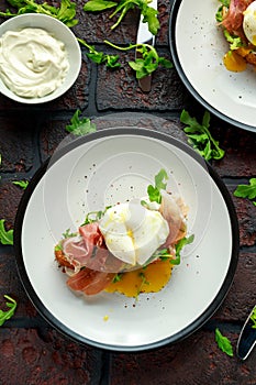 Bruschetta with cream cheese, wilde rucola, parma ham and poached egg served on white plate.