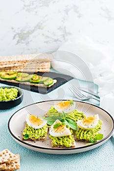 Bruschetta on crispy bread with avocado and boiled egg on a plate. Vertical view