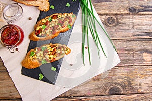 Bruschetta with feta cheese, dried tomatoes, olive oil and fresh microgreen herbs, on a stone plate on a wooden table.