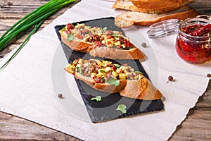 Bruschetta with feta cheese, dried tomatoes, olive oil and fresh microgreen herbs, on a stone plate on a wooden table.