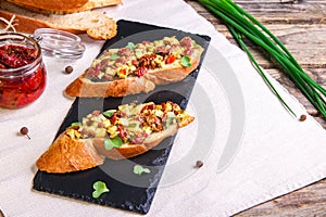 Bruschetta with feta cheese, dried tomatoes, olive oil and fresh microgreen herbs, on a stone plate on a wooden table.