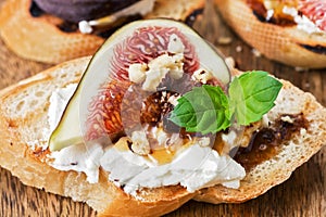 Bruschetta with goat cheese, figs, nuts and honey, selective focus. Italian appetizer close-up.