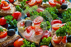 Bruschetta with green and black olives, feta cheese, cherry tomatoes, parsley and red pepper on black background