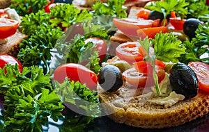 Bruschetta with green and black olives, feta cheese, cherry tomatoes, parsley and red pepper on black background