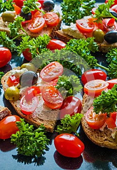 Bruschetta with green and black olives, feta cheese, cherry tomatoes, parsley and red pepper on black background