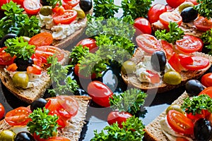 Bruschetta with green and black olives, feta cheese, cherry tomatoes, parsley and red pepper on black background