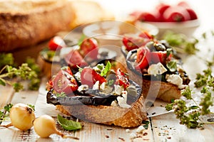 Bruschetta with grilled eggplant, cherry tomatoes, feta cheese, capers and fresh aromatic herbs on a wooden table. Delicious Medit