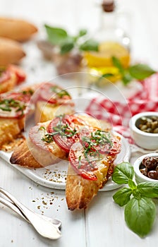 Bruschetta, grilled slices of baguette with mozzarella cheese, tomatoes, garlic and aromatic basil on a white wooden table