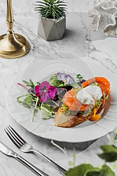 Bruschetta with Poached egg and fresh salmon , vegetarian salad with greens at the white plate on light marble background. Healthy