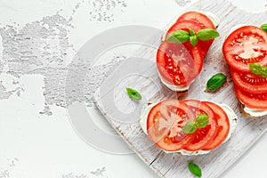 Bruschetta, toast with soft cheese, basil and tomatoes on a white wooden board. Italian healthy snack, food.