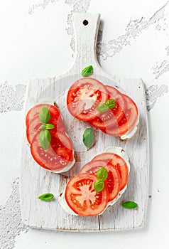 Bruschetta, toast with soft cheese, basil and tomatoes on a white wooden board. Italian healthy snack, food.