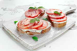 Bruschetta, toast with soft cheese, basil and tomatoes on a white wooden board. Italian healthy snack, food.