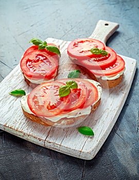 Bruschetta, toast with soft cheese, basil and tomatoes on a white wooden board. Italian healthy snack, food.