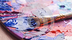 Brush and artist`s palette with mixed paints on wooden table, closeup