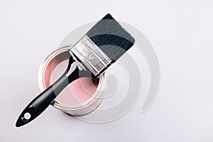 Brush with black handle on open can of pink paint on grey background.