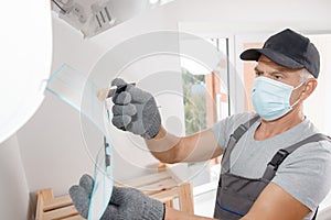 Brush cleaning Air conditioner from dust. Worker in gloves and medical mask checks filter
