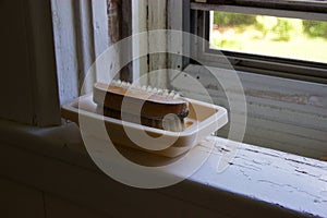 Brush, dish on white windowsill corner with chipped paint, screen