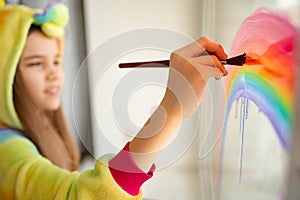 Brush. girl in kigurumi draws rainbow on window