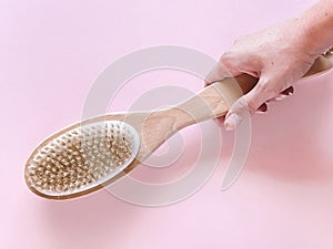 Brush with a handle for dry anti-cellulite massage or brushing in the hand of a girl in soft pink colors.  Beauty concept