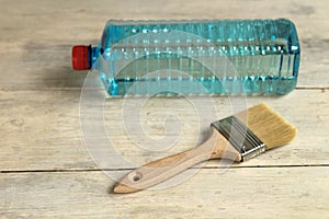 A brush lies next to a transparent plastic bottle with a solvent on an old white vintage wooden plank table. Place for text or