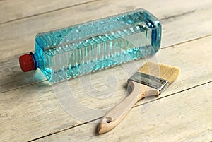 A brush lies next to a transparent plastic bottle with a solvent on an old white vintage wooden plank table. Place for text or