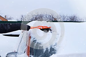 Brush in mans hand. Man clears windshield of orange car from snow. Car covered with snow. Winter problems of car drivers. Snowy