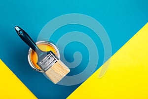 Brush on open can of yellow color paint on yellow and blue background.