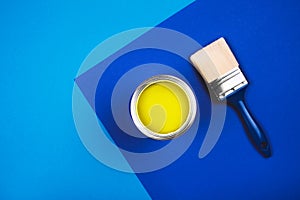 Brush and open can of yellow paint on blue background.