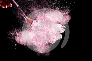 Brush with pink powder explosion on black background.Make-up and beauty concept
