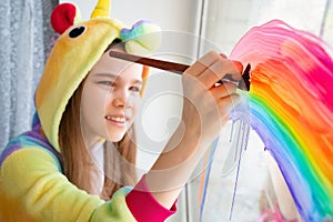 Brush. teen girl in kigurumi draws rainbow window photo