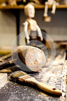 Brush and wooden hammer on a wooden table among the sawdust on the background of a finished wooden doll.